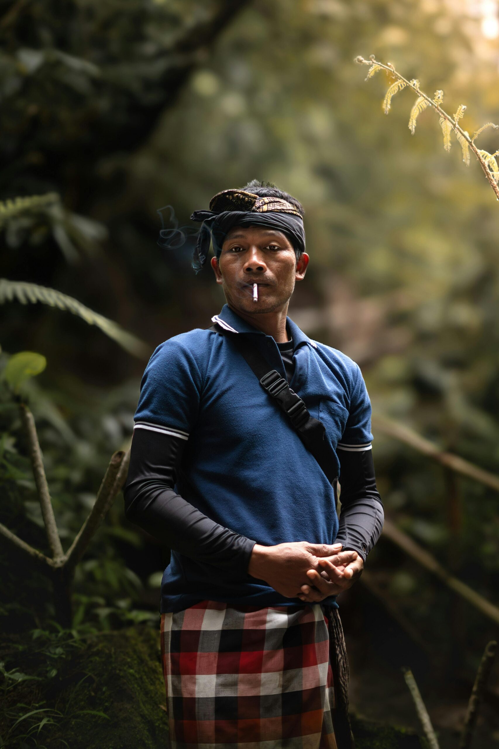 A man in traditional attire smokes in the lush jungle of Bali, Indonesia.